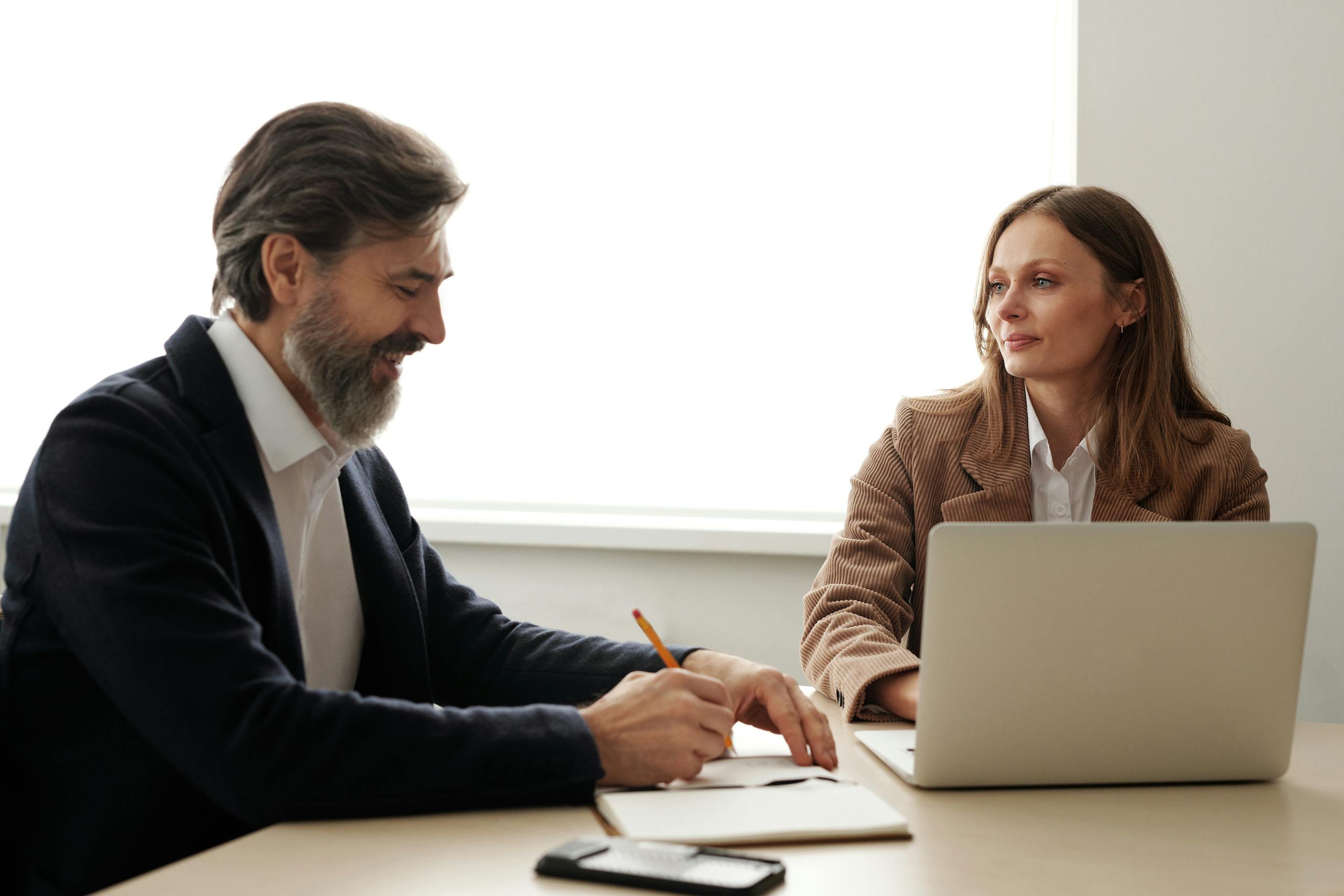 Man and Woman Sitting at Table Using Macbook