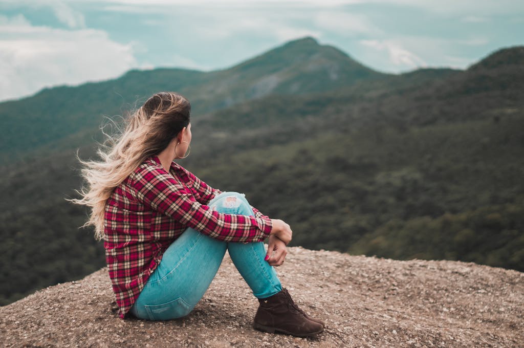 Side View Photo of Woman Sitting on Ground Overlooking a Hill